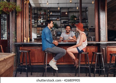 Group Of Young People Sitting In A Cafe And Talking. Young Men And Women Meeting At Cafe Table.