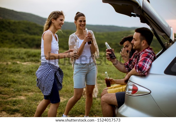 Group of young people sitting in the car trank\
during trip in the nature