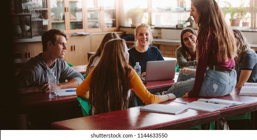 Group Of Young People Sitting In The Classroom And Talking. University Lecture Room With Students Chatting During Break.