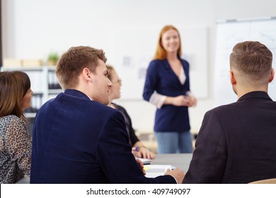 Group Of Young People In Small Office Staff Meeting From Back Of Man In Jacket Looking At Co-workers Discussing Something