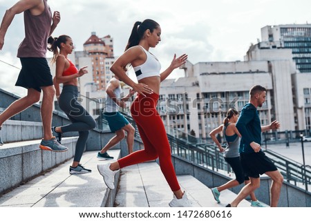 Group of young people in sports clothing jogging while exercising on the stairs outdoors                    