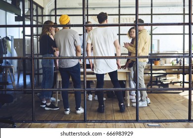 Group Of Young People Standing Around Table In Contemporary Office And Talking. Group Of Stylish Creative Colleagues Brainstorming At Meeting. 