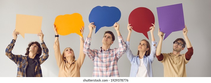 Group Of Young People Standing On Gray Studio Background, Looking Up At Multicolored Empty Cardboard And Paper Mockup Speech Bubbles, Giving Feedback, Sharing Important Message, Expressing Own Opinion