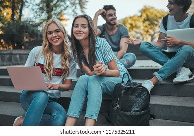 Group Of Young People Are Studying Together In University. Students Outdoors Sitting On Stairs.