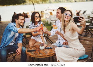 Group of young people toast with cocktails and making selfie at a summer bar during the day