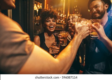 Group Of Young People Toasting Drinks At Nightclub. Young Men And Women Having Fun At Lounge Bar.