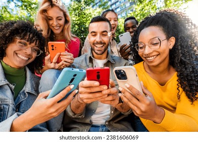 Group of young people using smart mobile phone outdoors - Happy friends with smartphone laughing together watching funny video on social media platform - Tech and modern life style concept 