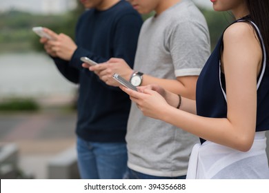 Group Of Young People Using Smartphones When Standing Outdoors