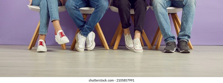 Group of young people waiting in line. College students, classmates and friends in jeans and sneakers sitting in a row. Banner header background. Cropped shot, low section, legs and feet on the floor - Powered by Shutterstock