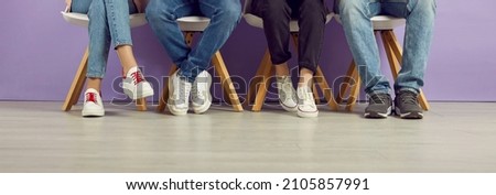 Group of young people waiting in line. College students, classmates and friends in jeans and sneakers sitting in a row. Banner header background. Cropped shot, low section, legs and feet on the floor 商業照片 © 