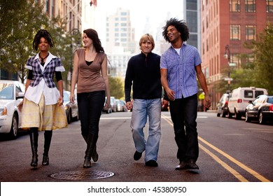 A Group Of Young People Walking Down A Street In A Large City