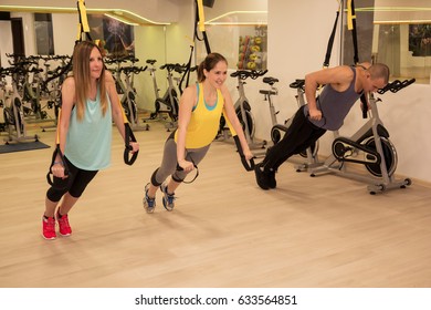 Group Of Young People Working Out On Suspension Straps In Gym. Team Of Athletes Having TRX Sports Training During Exercise Class.