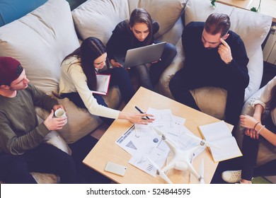 Group Of Young Pupils Is Preparing For Exams While Sharing Opinions, Reading Materials On Marketing Research  Sitting In Coworking. Teamwork Cooperates Using Computers, Books And Internet Networking