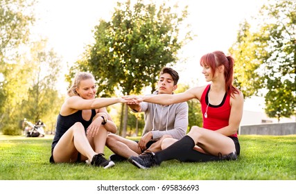 Group Of Young Runners Sitting On Grass Stacking Hands.