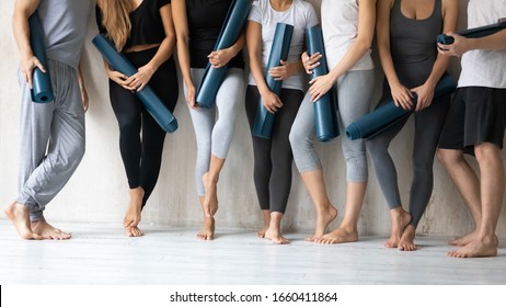 Group of young slim sporty girls and guys wearing comfy stylish sportswear holding personal carpets leaned on wall background waiting for yoga class. Concept of hobby, healthy lifestyle and wellness