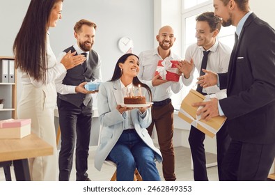 Group of young smiling business people congratulating their happy female colleague on her birthday giving her birthday cake and present gift boxes on workplace in office. Corporate party - Powered by Shutterstock