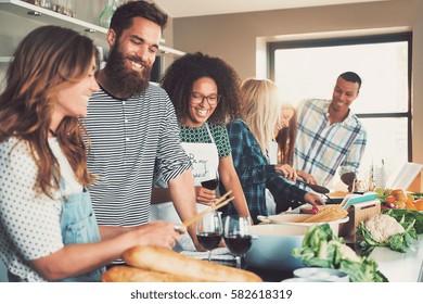 Group of young smiling cheerful friends cooking some meal at kitchen with wine glasses, they drink simultaneously. - Shutterstock ID 582618319