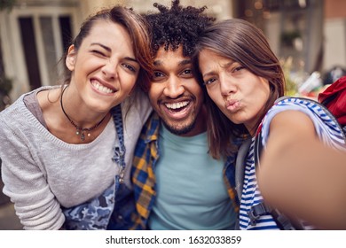 group of young smiling friends looking to phone and taking sefie outdoor.
