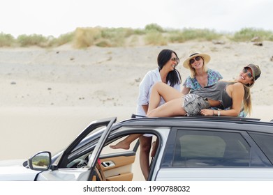 A Group Of Young Spanish Girls Smiling And Having Fun On The Beach While Laying On Top Of Their Car