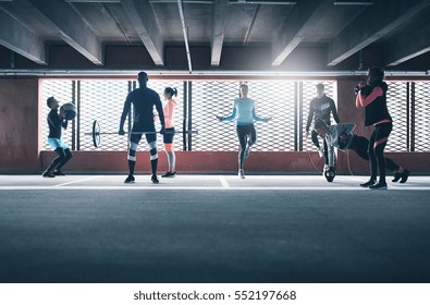 Group Of Young Sporting Adults Training On Athletic Field Against Barred Window. 