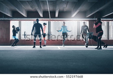 Group of young sporting adults training on athletic field against barred window. 