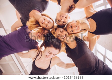 Group of young sportive people standing in a circle, laughing, hugging indoors, having fun, hands