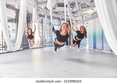 Group of young sportive women stretching on aerial yoga hammocks in gym with panoramic windows - Powered by Shutterstock