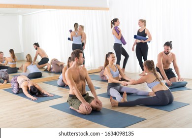 Group Of Young Sporty Attractive People In Yoga Studio, Relaxing And Socializing After Hot Yoga Class. Healthy Active Lifestyle, Working Out Indoors.