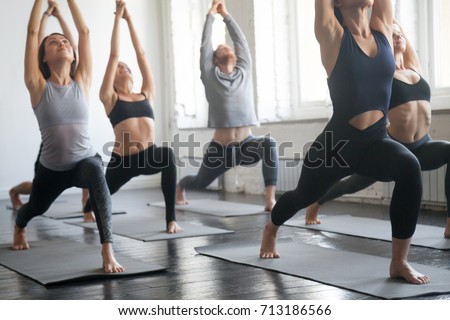 Group of young sporty attractive people practicing yoga lesson with instructor, standing together in Virabhadrasana 1 exercise, Warrior one pose, working out, full length, studio background, close up 