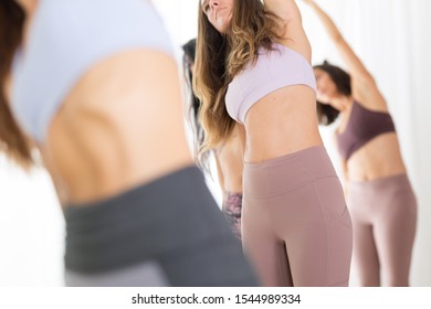 Group of young sporty attractive women in yoga studio, practicing yoga lesson with instructor, standing together in half moon asana pose. Healthy active lifestyle, working out indoors in gym. - Shutterstock ID 1544989334