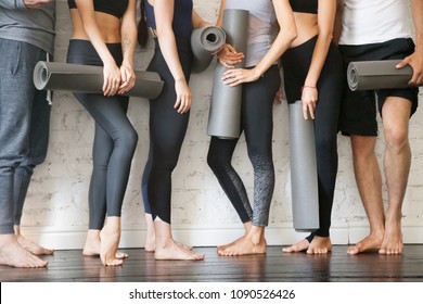 Group of young sporty people with fitness yoga exercise mats standing beside white wall. Rest from fitness activity, time to recover strength. Sport instructors inviting for class. Close up view photo