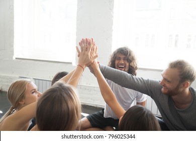 Group of young sporty people giving a high five, slapping the palms with hands raised above, well done concept, team training for spirit, fun, and motivation, victory or celebration gesture