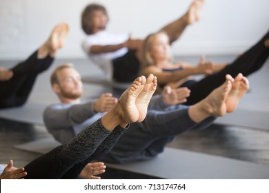 Group of young sporty people practicing yoga lesson with instructor, stretching in Paripurna Navasana exercise, balance pose, working out, indoor close up image, studio, focus on feet  - Powered by Shutterstock