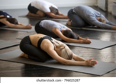 Group of young sporty people practicing yoga lesson with instructor, stretching in Child exercise, Balasana pose, working out, indoor close up, students training in club, studio