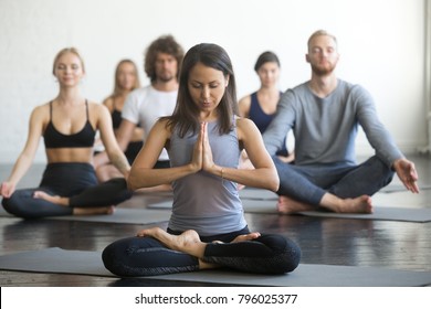 Group of young sporty people practicing yoga lesson with instructor, sitting in Padmasana exercise, Lotus pose with mudra gesture, working out, students training in club, indoor full length, studio - Shutterstock ID 796025377