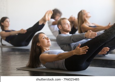 Group of young sporty people practicing fitness lesson with instructor, doing warming up exercise, boat pose, working out, students training in club, friends at fitness lesson, indoor, studio - Powered by Shutterstock