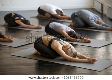Group of young sporty people practicing yoga lesson, doing Child exercise, Balasana pose, working out, indoor full length, students training in club, studio
