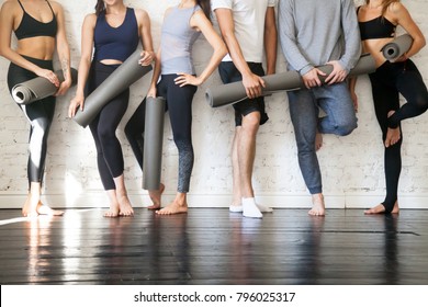 Group of young sporty people standing at wall. Students taking a rest from fitness activity, time to recover strength, waiting for a lesson to start in loft studio, close up. Healthy lifestyle concept
