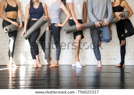 Group of young sporty people standing at wall. Students taking a rest from fitness activity, time to recover strength, waiting for a lesson to start in loft studio, close up. Healthy lifestyle concept