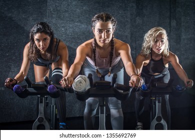Group of young sporty women riding cycling bikes during spinning class indoors