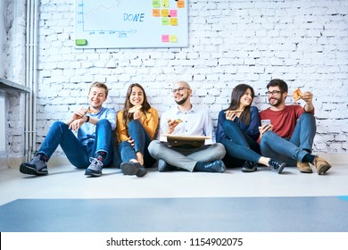 Group of young startup entrepreneurs enjoying their lunch break. University students sitting on floor eating pizza - Shutterstock ID 1154902075