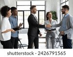 Group of young start-up founders meeting experienced business trainer at networking event in modern loft workspace. Diverse team of smiling office workers welcoming new colleague to company