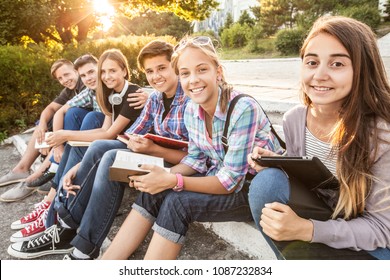 Gruppe junger Schüler mit Büchern und Gadgets sitzen auf den Stufen im Park
