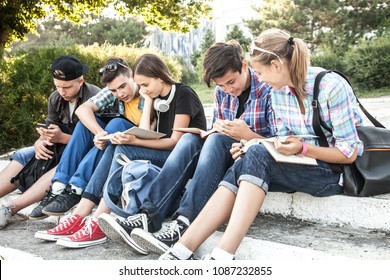 Gruppe junger Schüler mit Büchern und Gadgets sitzen auf den Stufen im Park