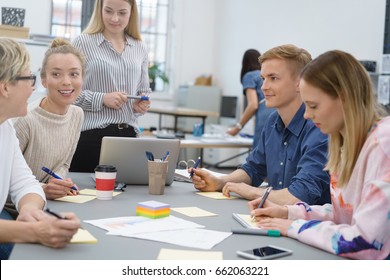 Group Of Young Students Or Business Colleagues Sitting Around A Table In An Office With Memo Pads And Notes As They Have A Brainstorming Session