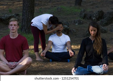 Group of young students following meditation class lead by female teacher in forest park. Woman guiding mindfulness exercise with hand on man's head. Inner self connection, inspiration moment concepts - Powered by Shutterstock