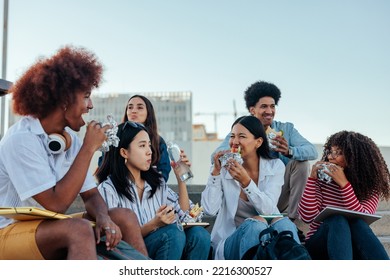 A Group Of Young Students Are Outside On The Campus Having A Lunch Break Together And Eating Sandwiches.