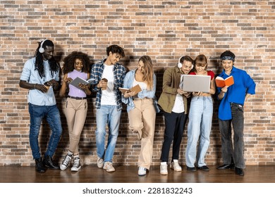 Group of young students posing in front of a brick wall, happy and smiling expressions holding books, diaries, laptops