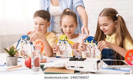 A group of young students are working together to build robots in a classroom setting. They are being guided by a teacher, who is standing behind them and observing their progress. - Powered by Shutterstock