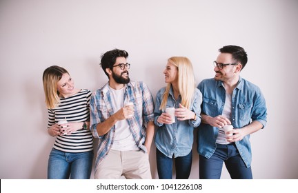 Group of young stylish happy people leaning against the wall and talking while drinks coffee in the paper cup. - Powered by Shutterstock